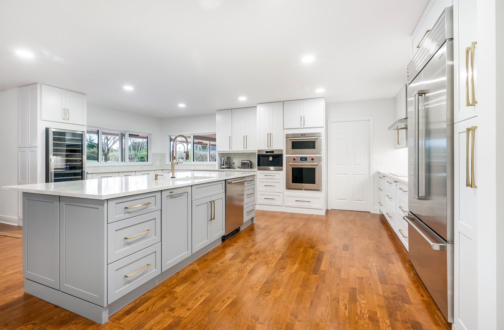 Bright modern white kitchen with island, hardwood floors, stainless steel appliances, and recessed lighting