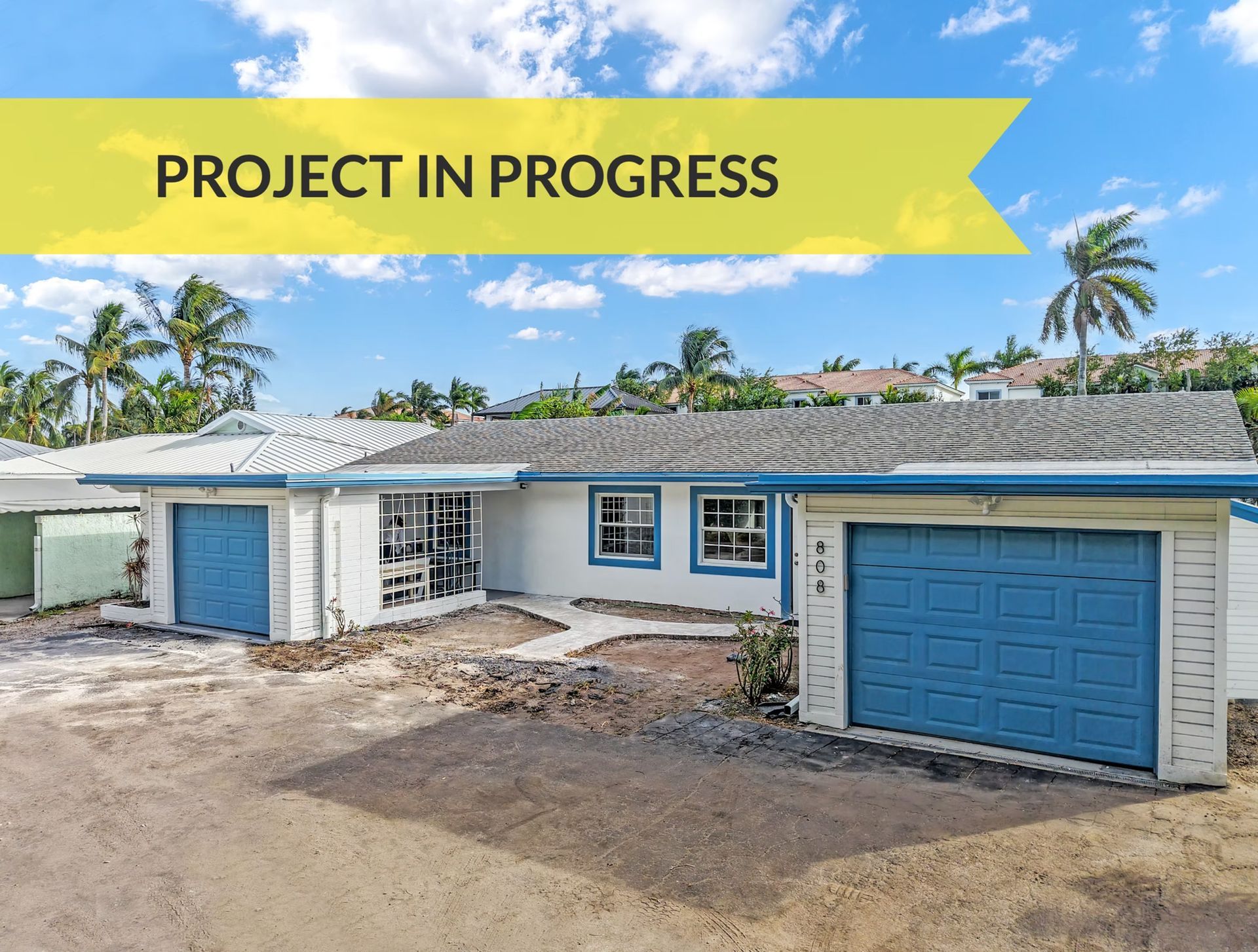 House exterior under renovation with blue garage doors and a yellow “PROJECT IN PROGRESS” banner