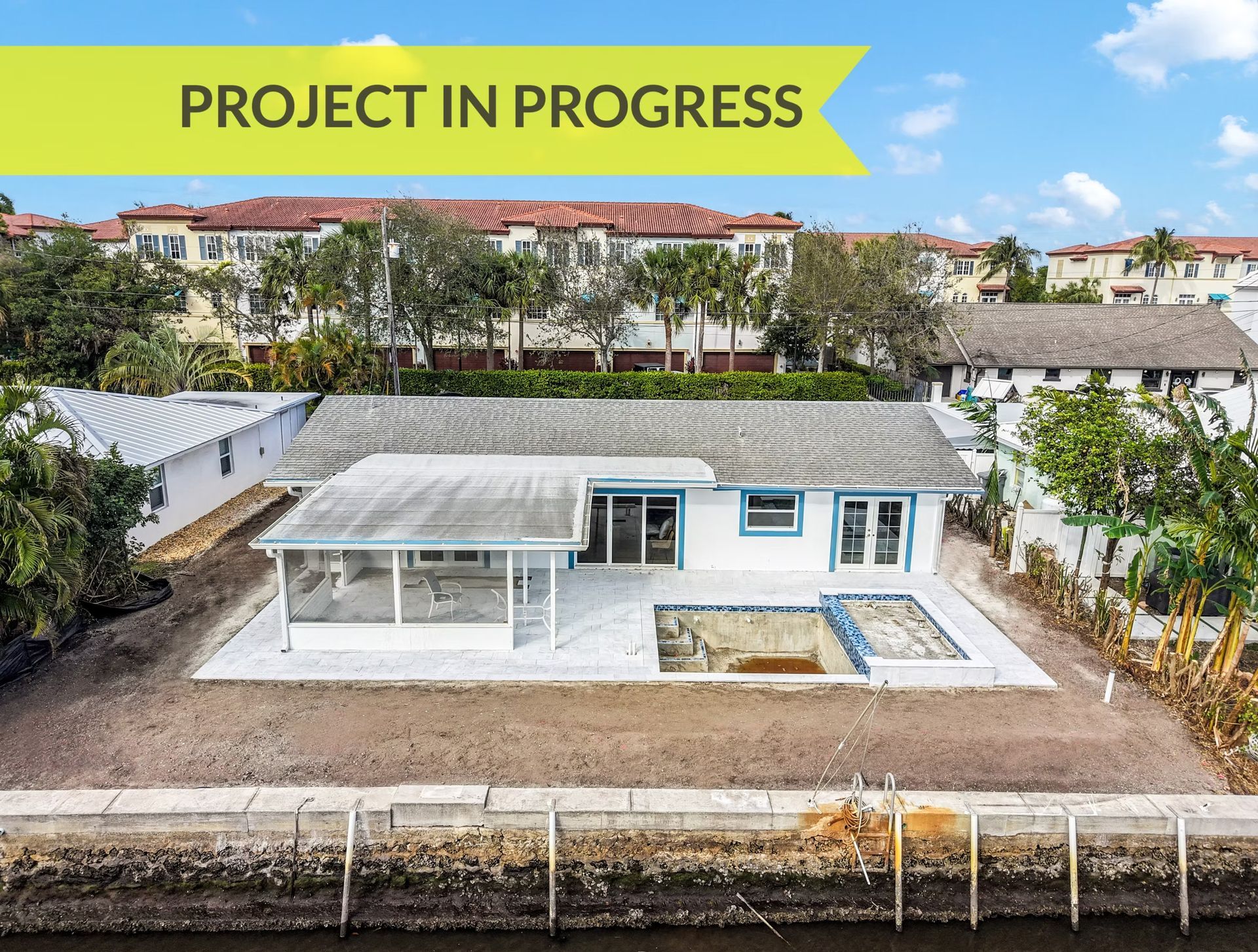 Aerial view of a white house under construction with a “PROJECT IN PROGRESS” banner and a pool area.