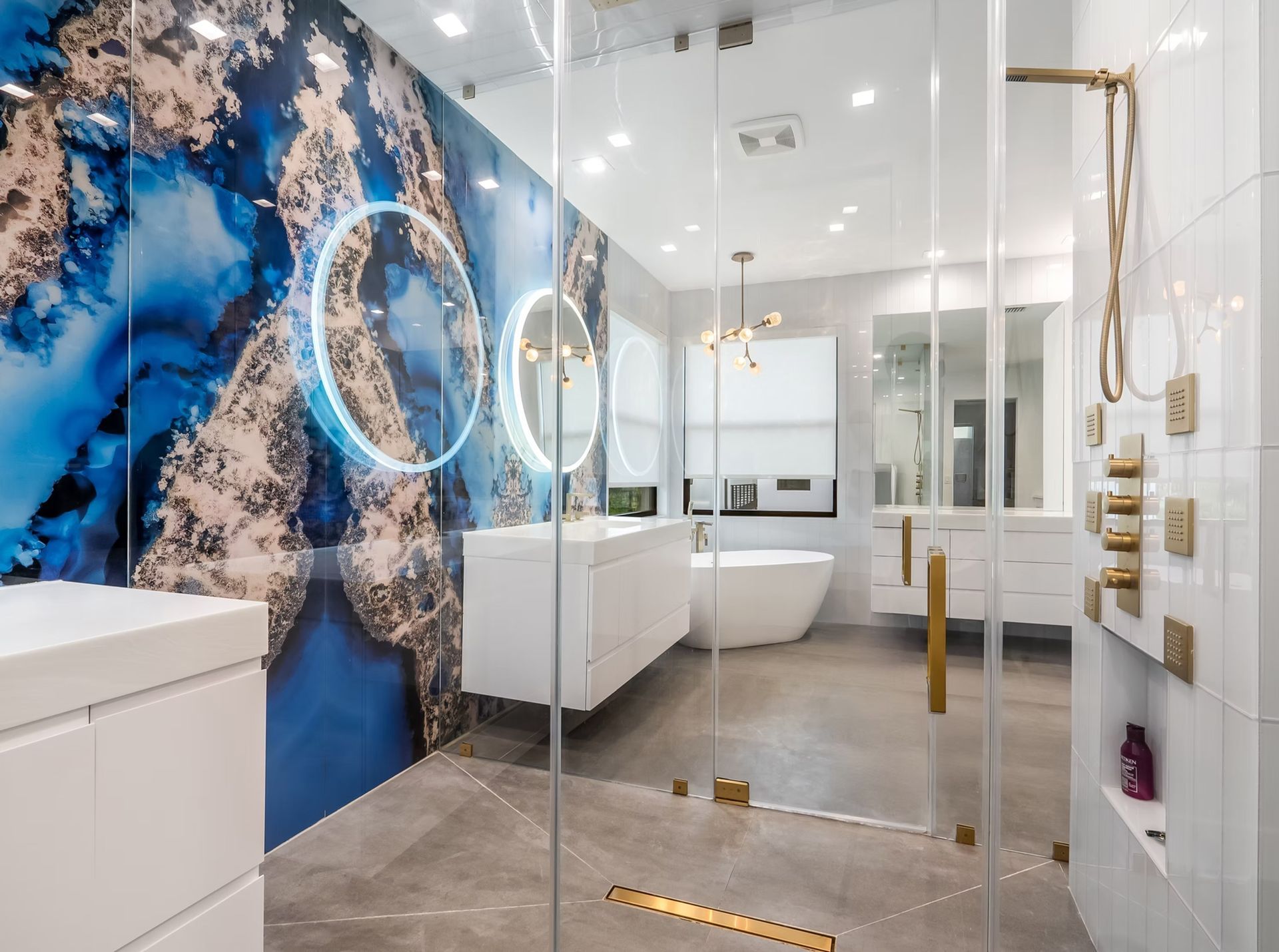 Modern luxury bathroom with blue marble wall, glass shower, white sink, and gold fixtures