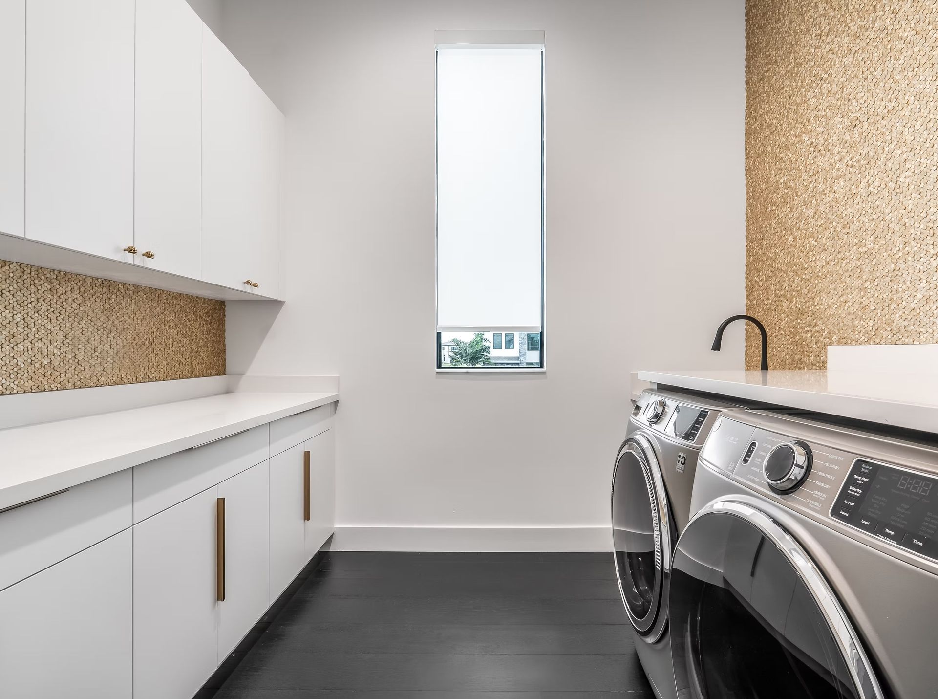Bright laundry room with white cabinets, black countertops, and a washer and dryer along the right wall.