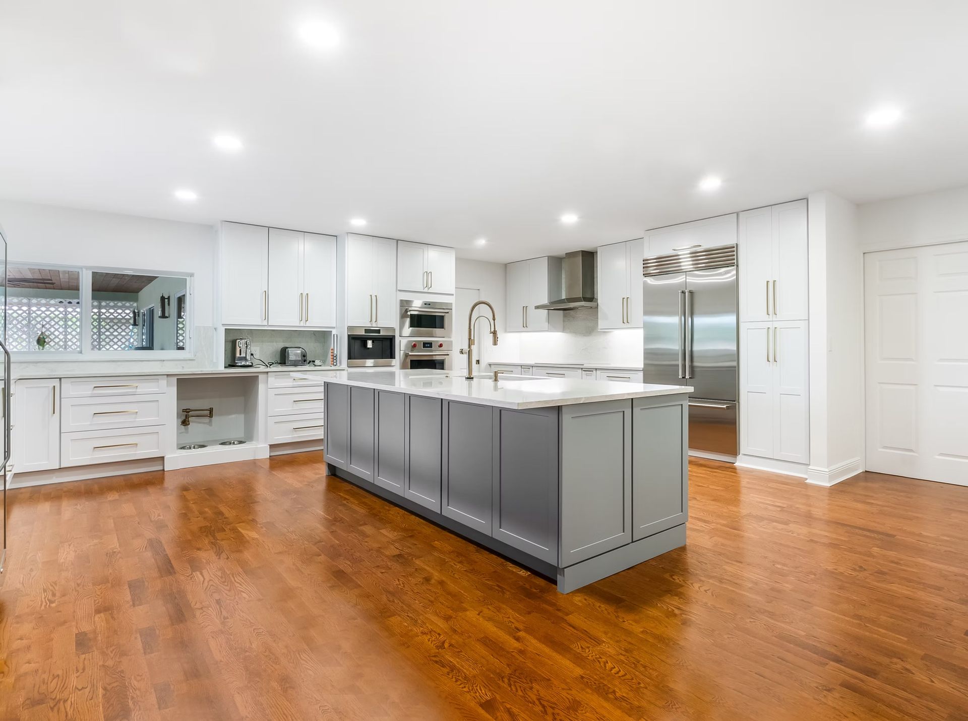 Modern white kitchen with gray island, stainless appliances, and warm hardwood floors