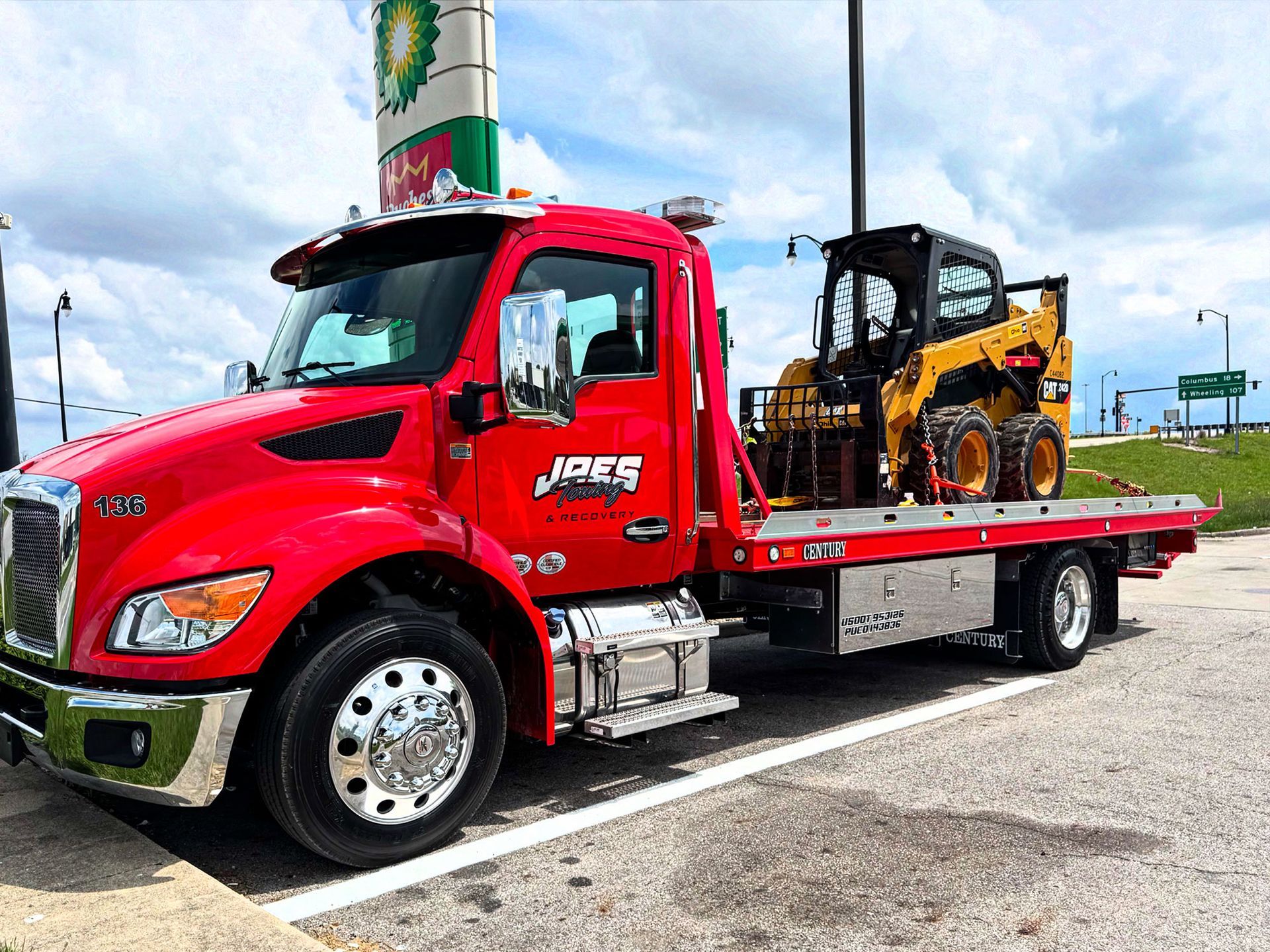 Red flatbed tow truck carrying a yellow construction vehicle in a parking lot