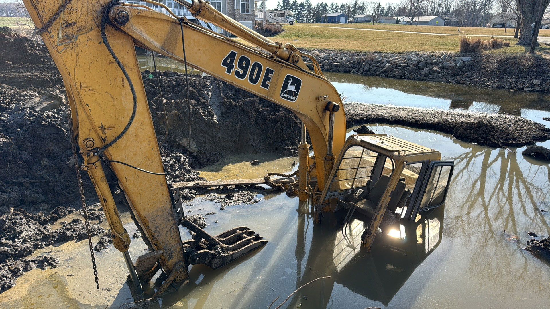 Yellow excavator working in muddy water beside a creek on a rural construction site