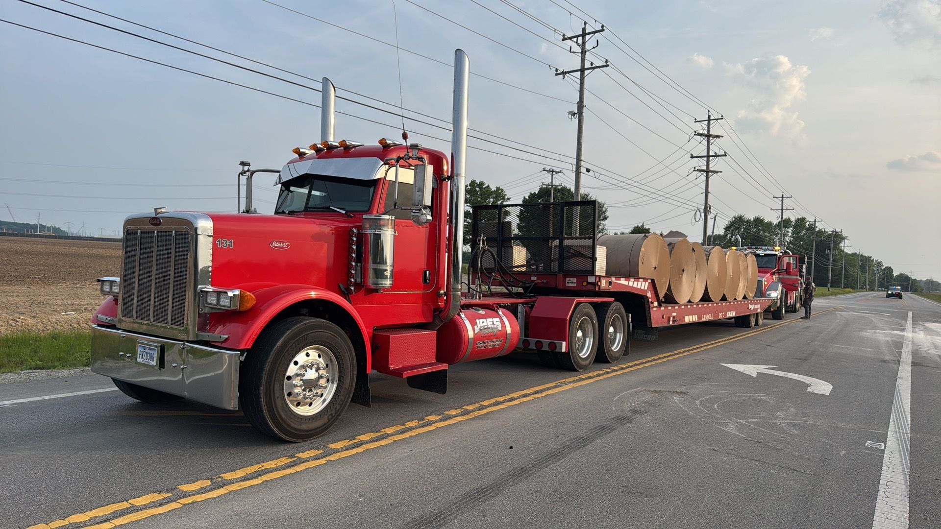 Red semi truck hauling large cylindrical loads on a flatbed along a rural road