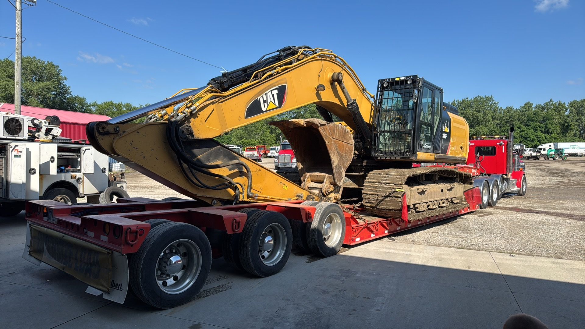 Yellow excavator loaded on a red lowboy trailer at an outdoor work site