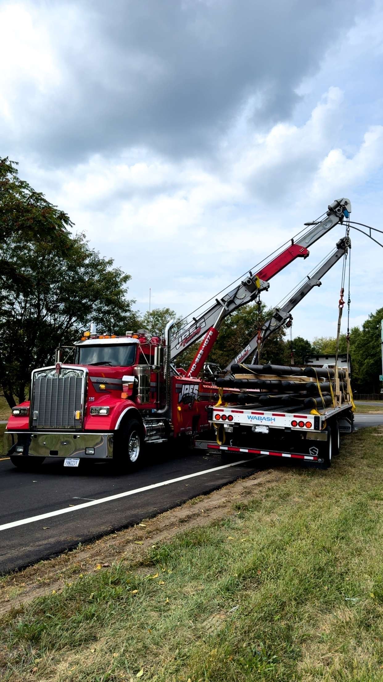 Red tow truck lifting a damaged car on a roadside under cloudy sky