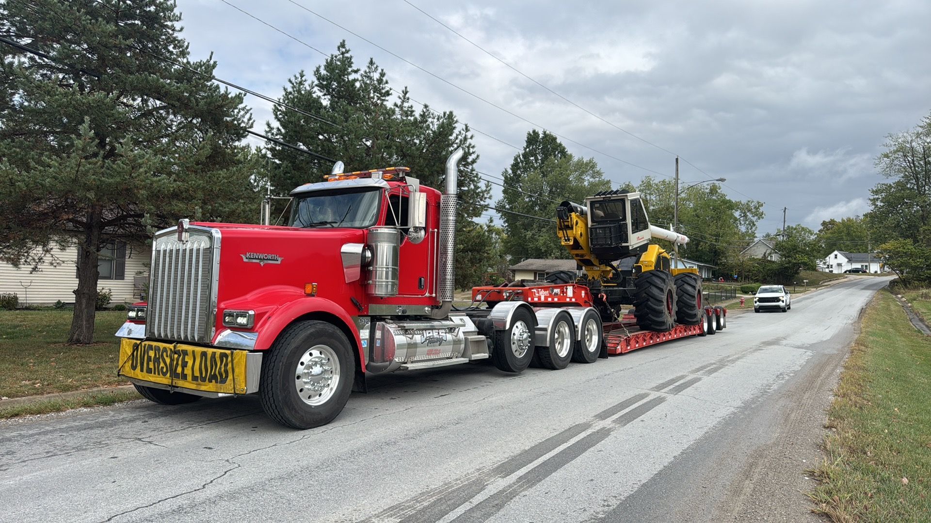 Red semi-truck hauling a yellow bulldozer on a trailer along a rural road under cloudy skies