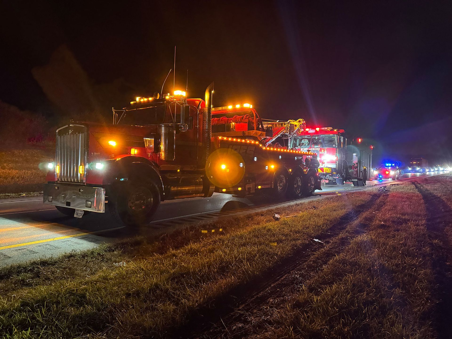 Tow trucks with flashing amber lights line a wet roadside at night