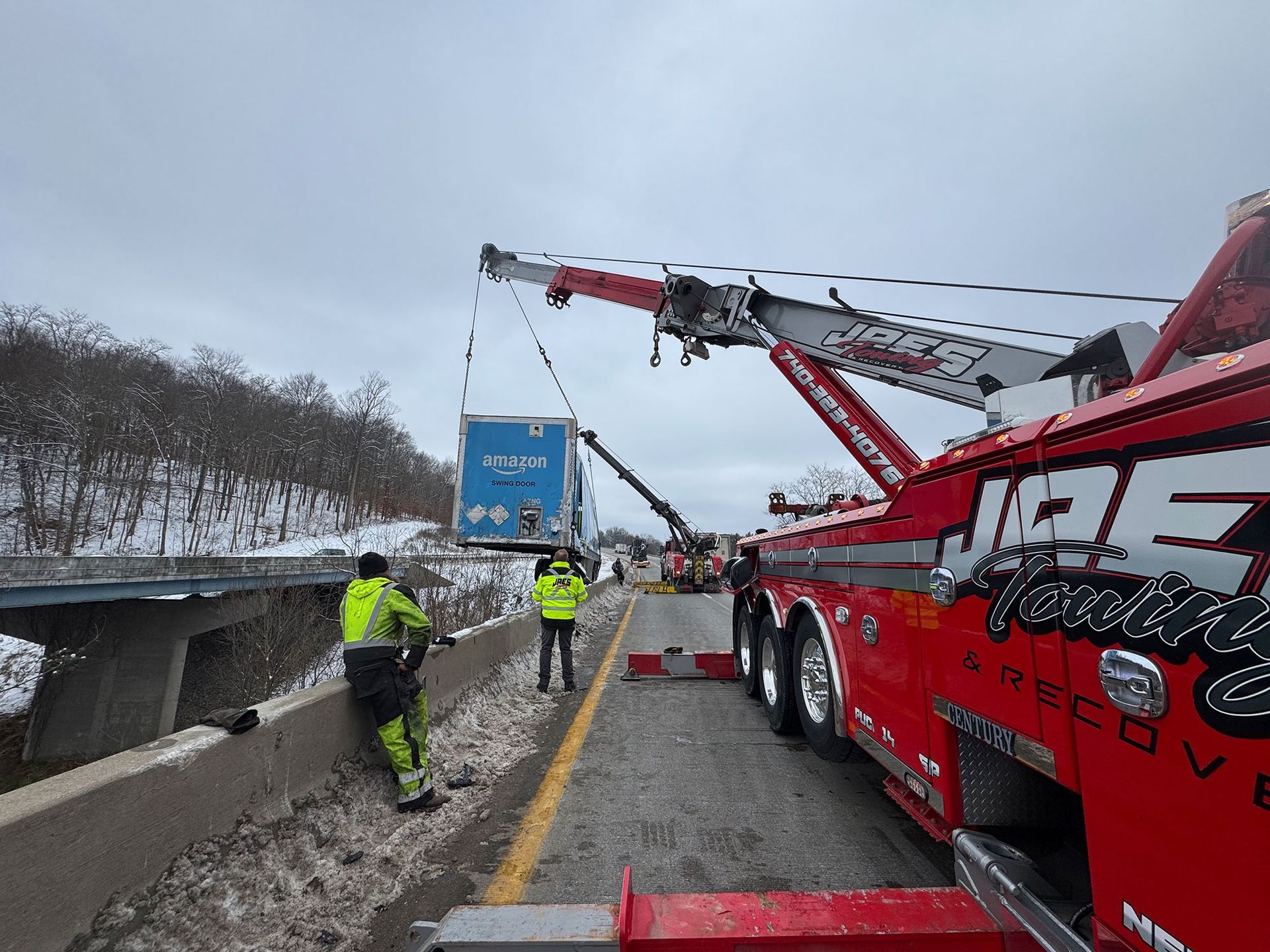 Tow truck crew recovering a blue truck on a snowy highway shoulder after a roadside crash