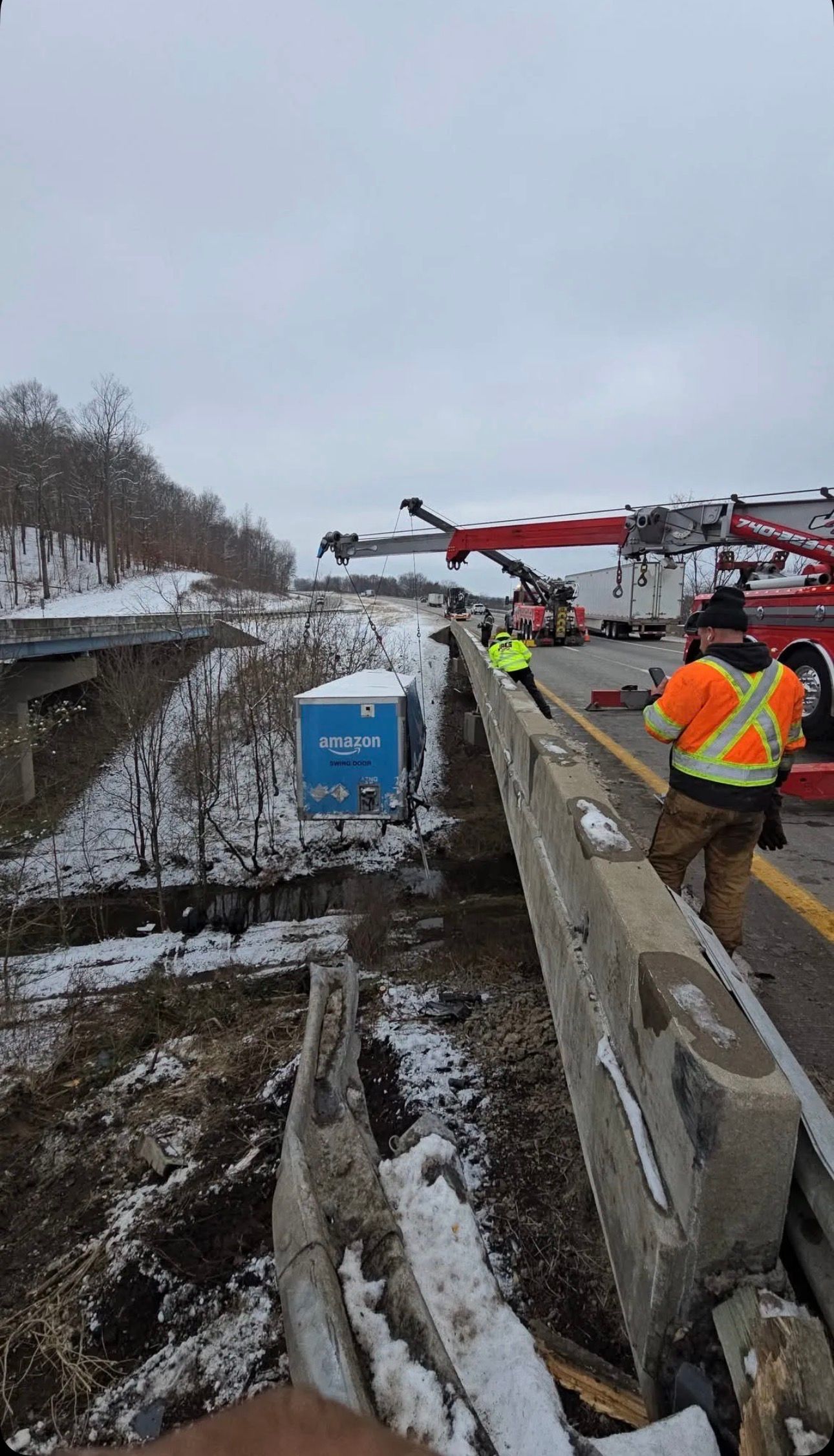 Rescue crew near a red helicopter on a snowy roadside beside a collapsed bridge or embankment
