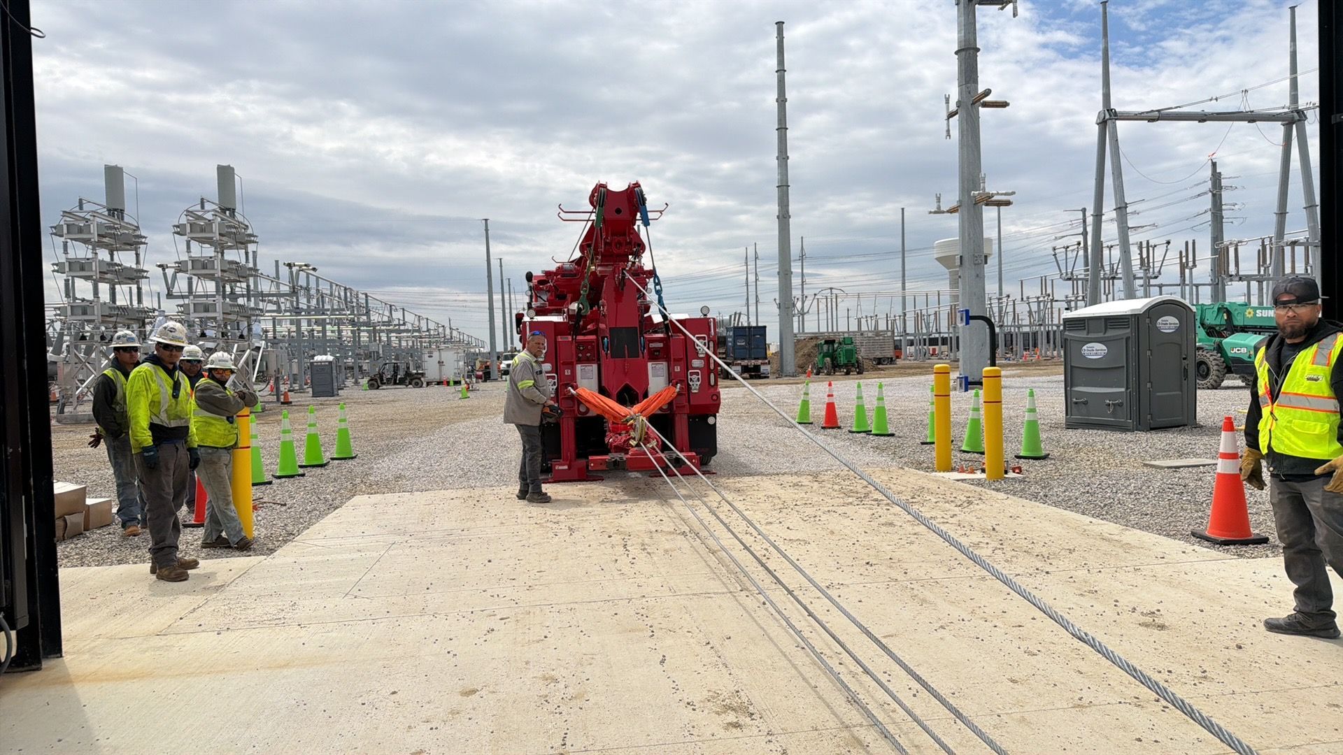 Red utility machine on a dirt road in an industrial electrical substation, workers in high-vis gear nearby