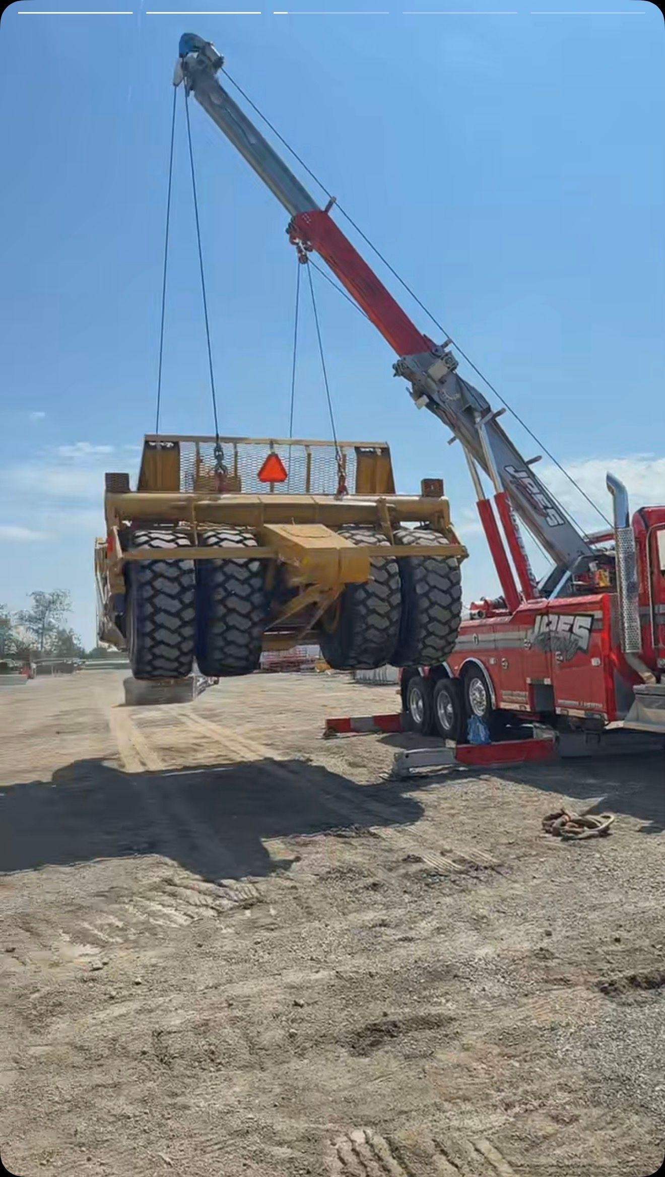 Crane lifting a large heavy-duty vehicle frame at a construction site under a clear blue sky