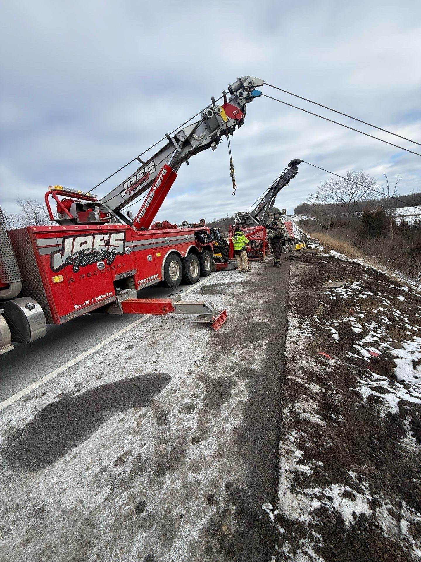 Red tow truck lifting a worker amid a roadside accident scene on a snowy shoulder.