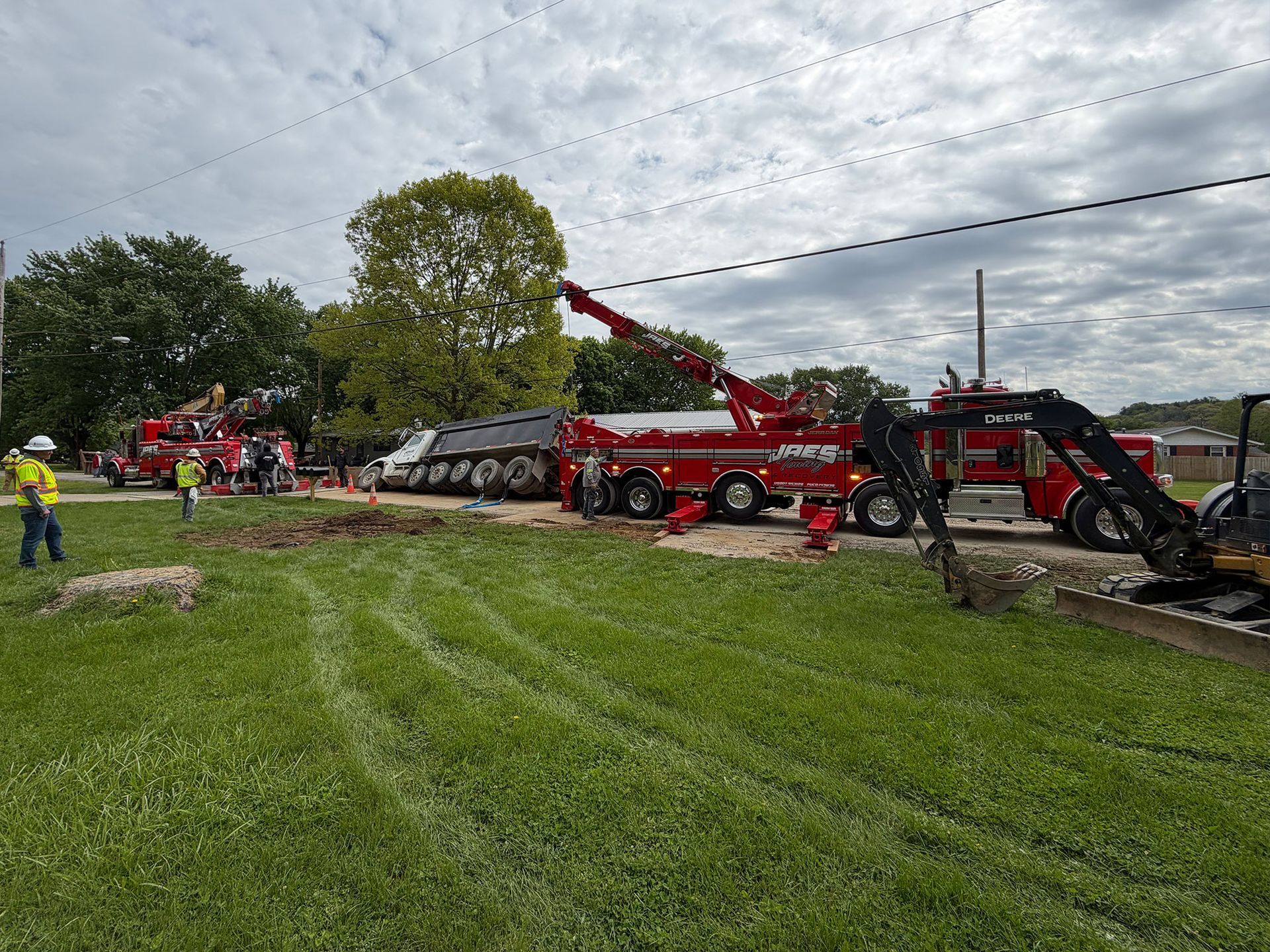 Red rescue truck and firefighters at a roadside scene, with a car overturned in the ditch near a grassy field