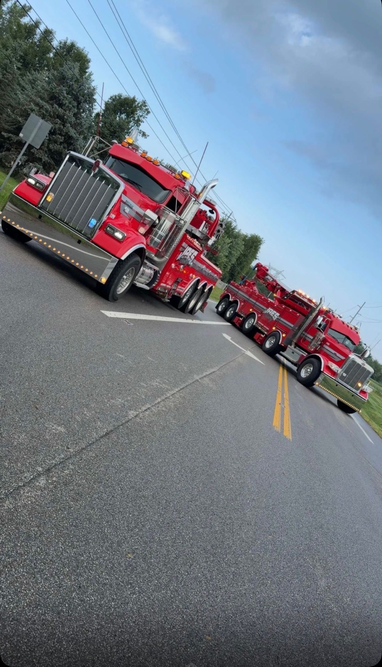 Red fire trucks parked diagonally along a road under a cloudy sky