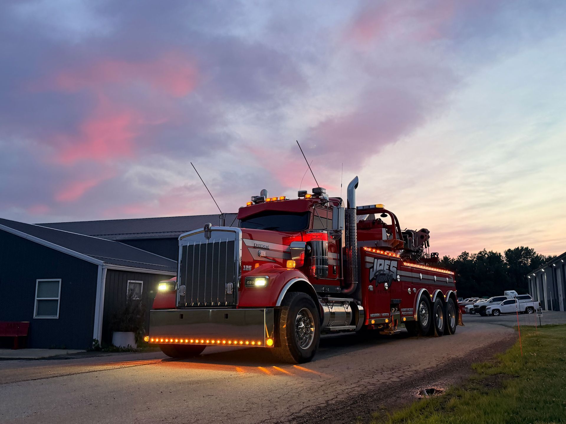 Red tow truck with flashing lights parked on a street at dusk near houses