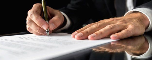 lawyer signing important legal document on black desk