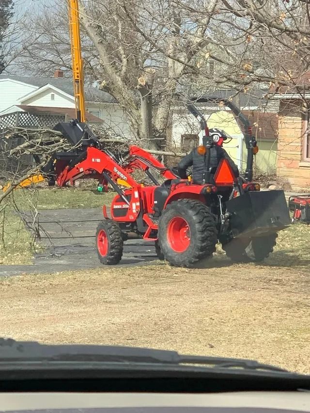 A red tractor with a front loader is clearing debris from a driveway, operator in the seat.