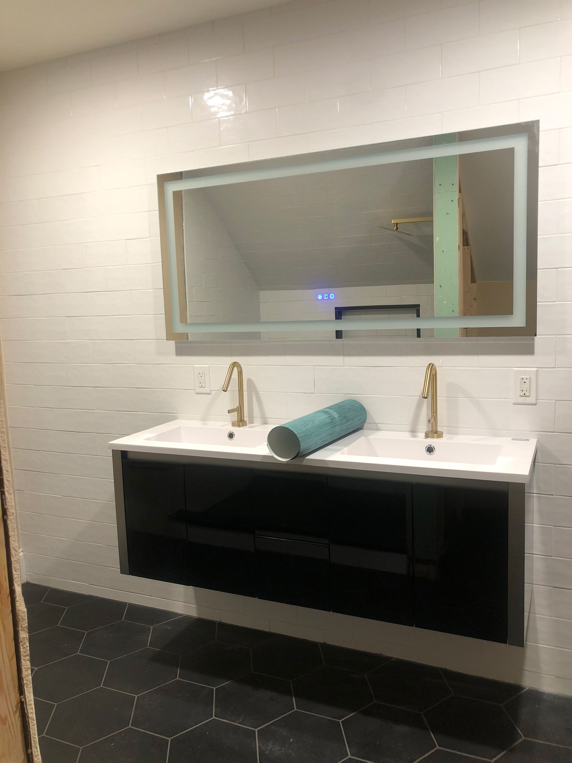 Floating vanity with double sinks, gold faucets, and a backlit mirror in a bathroom.