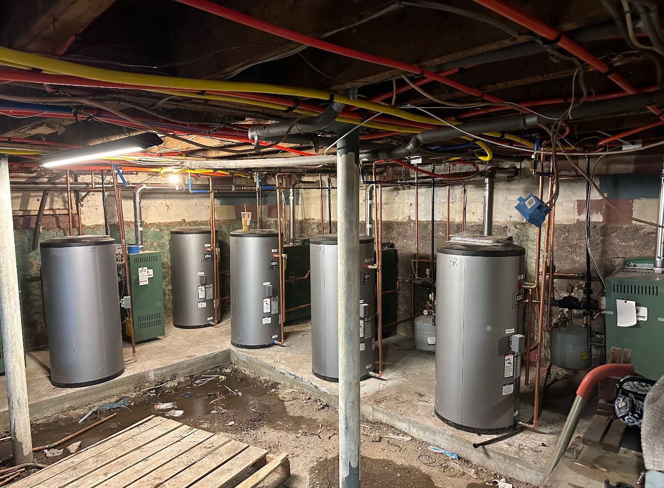 Basement with multiple water tanks, pipes, and electrical wiring. Concrete floor, dim lighting.