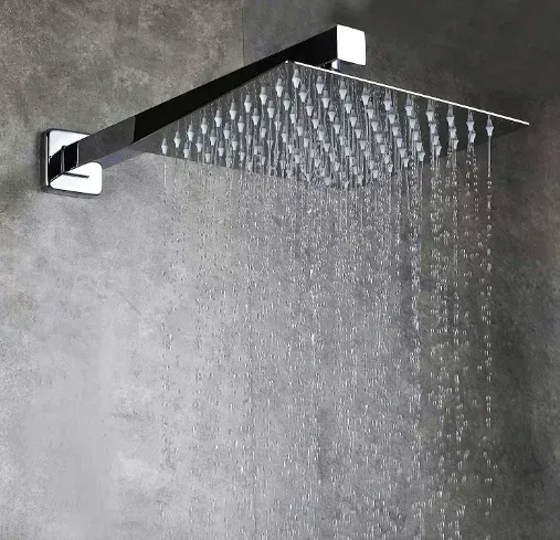Square chrome rain shower head with water flowing, mounted on a gray wall.