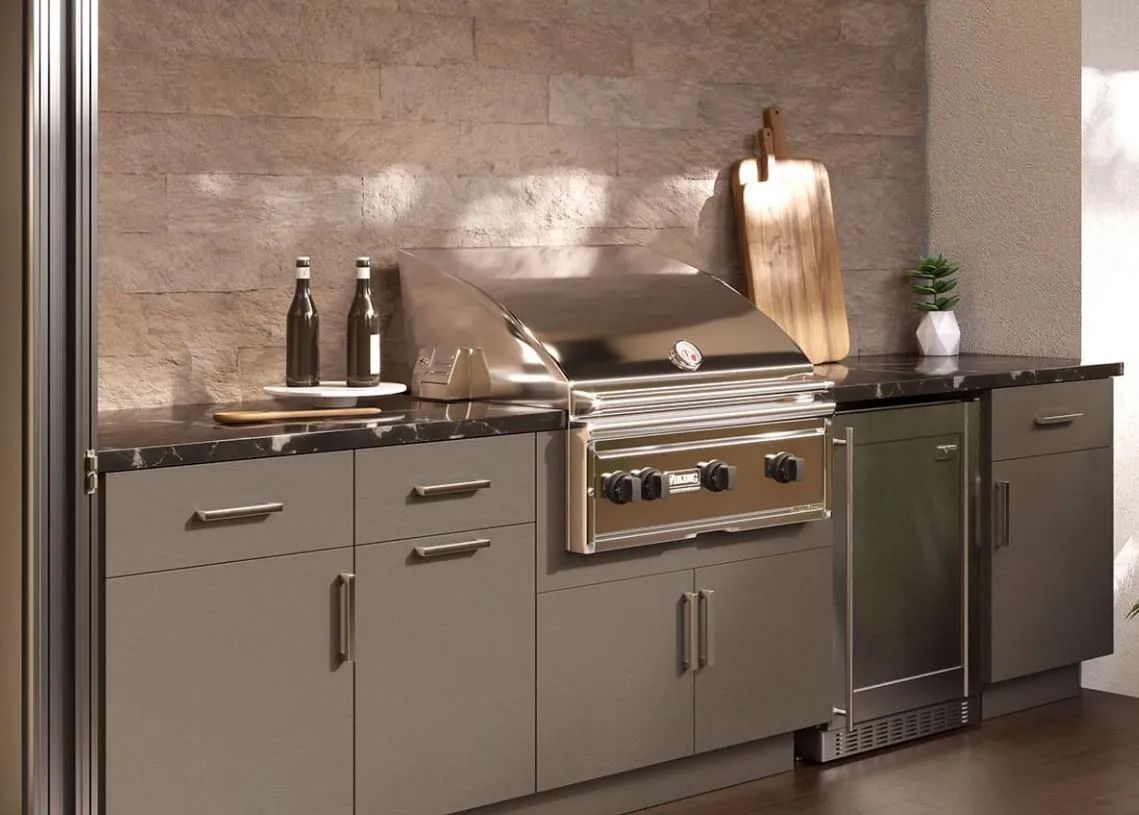 Modern outdoor kitchen with stainless steel grill, sink, and cabinets against a stone wall