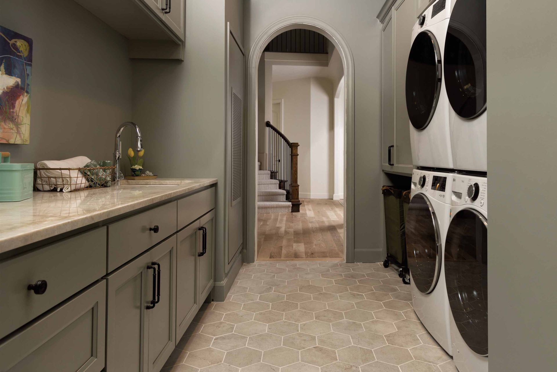 Laundry room with front-loading washer and dryer, gray cabinets, and a doorway to a hallway beyond.