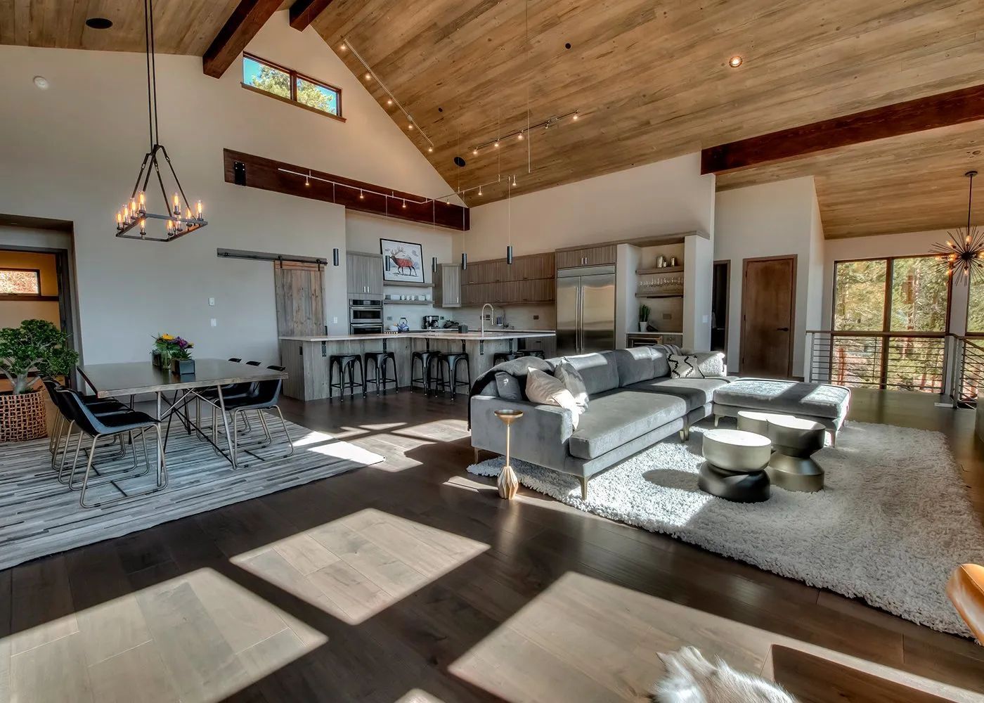 Bright modern living room with vaulted wood ceiling, kitchen bar, sofas, and sunlight on the floor