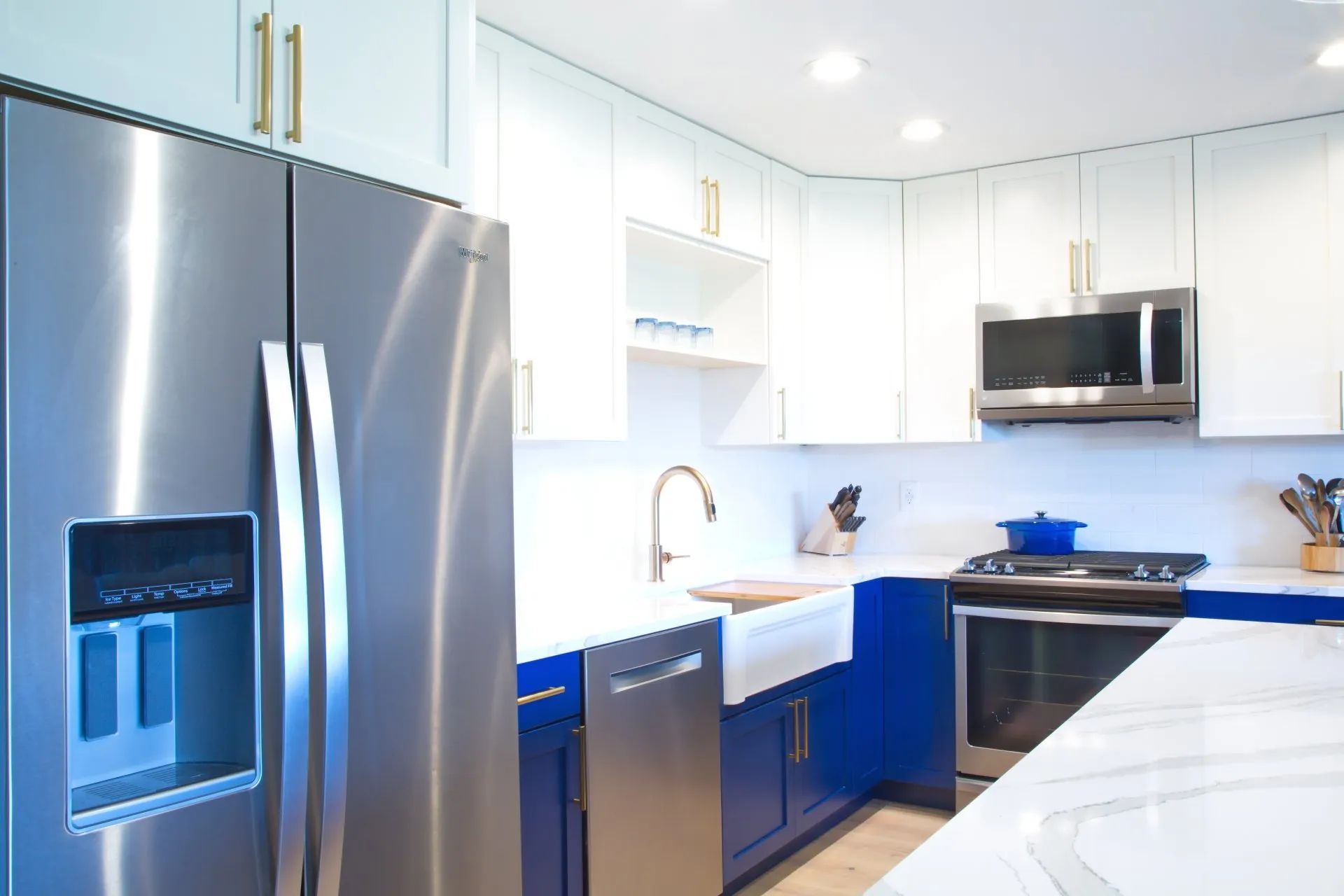 Modern white kitchen with stainless steel appliances and blue lower cabinets, brightly lit.