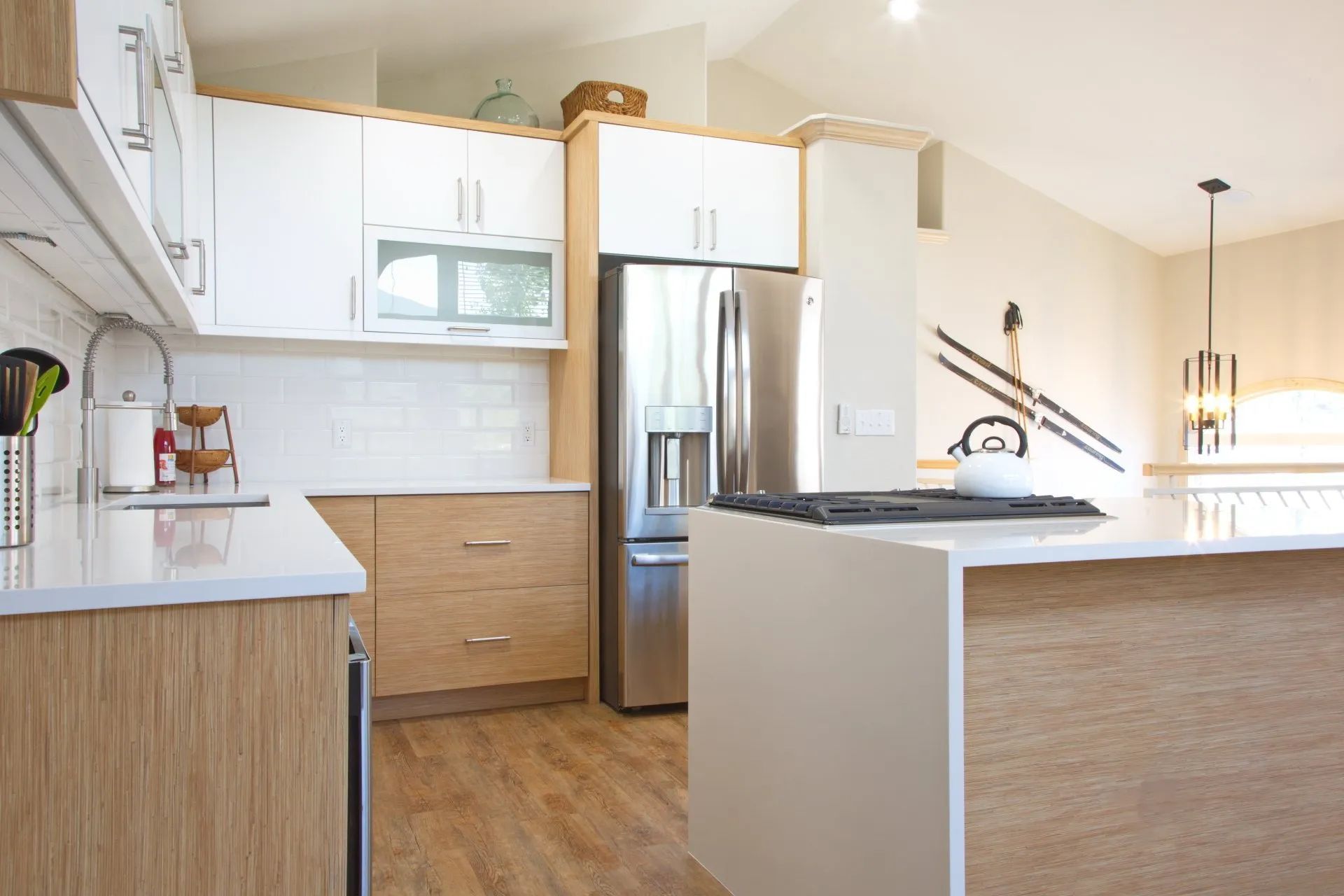 Modern white kitchen with wood cabinets, stainless fridge, and a peninsula island with pendant lights