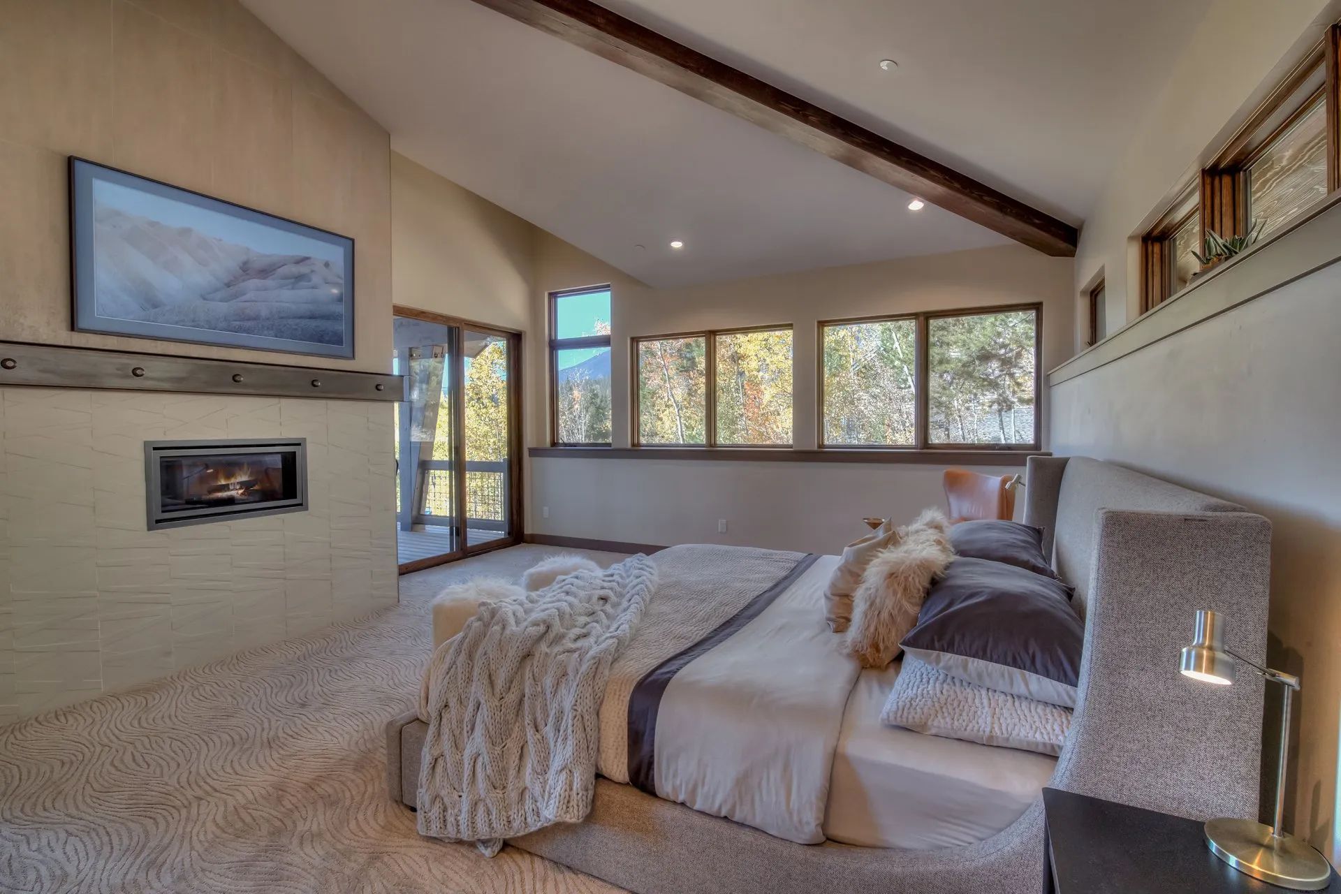 Modern bedroom with fireplace, large windows, vaulted ceiling, and neutral bedding