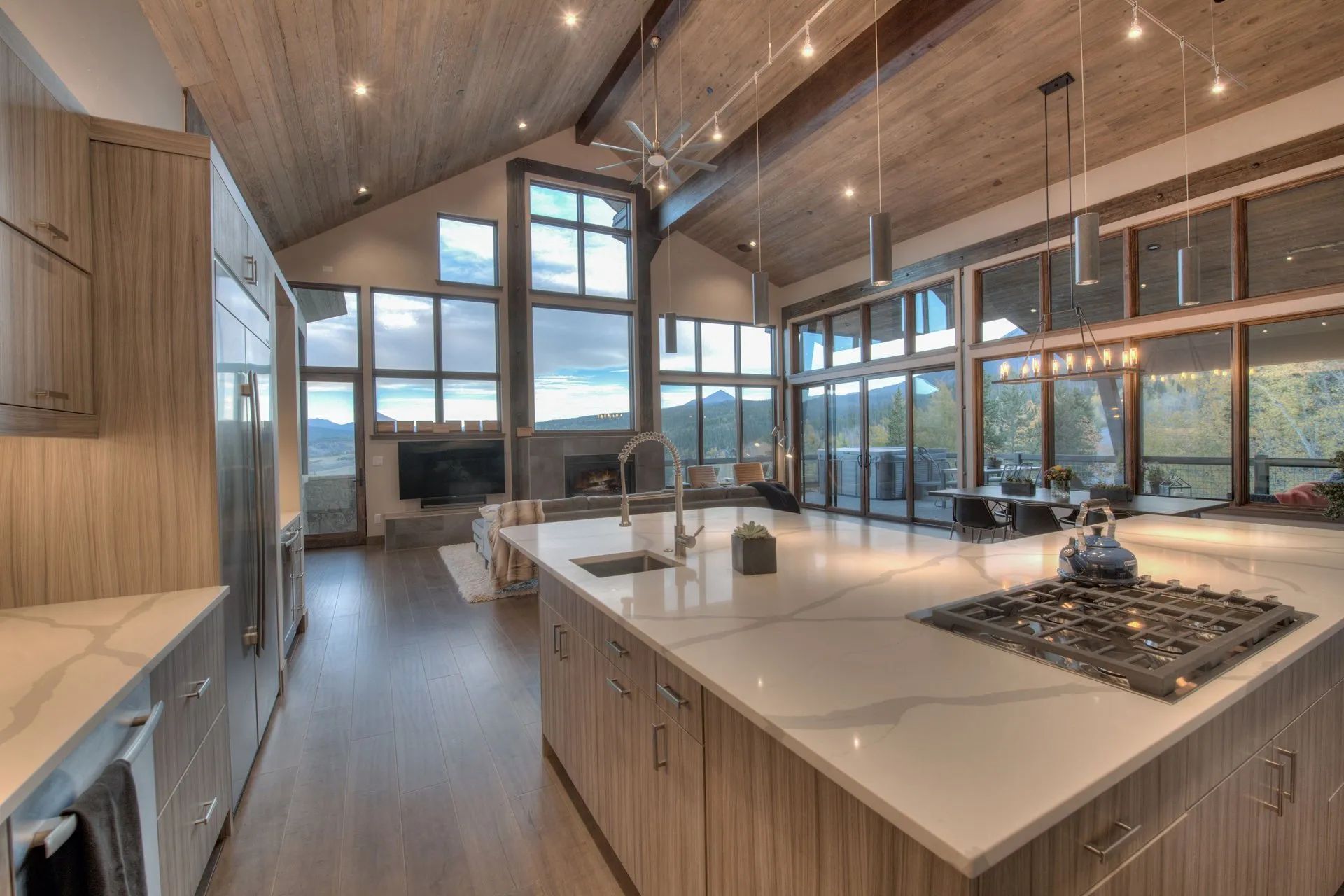 Modern open-concept kitchen with wood cabinets, large island, high ceilings, and floor-to-ceiling windows