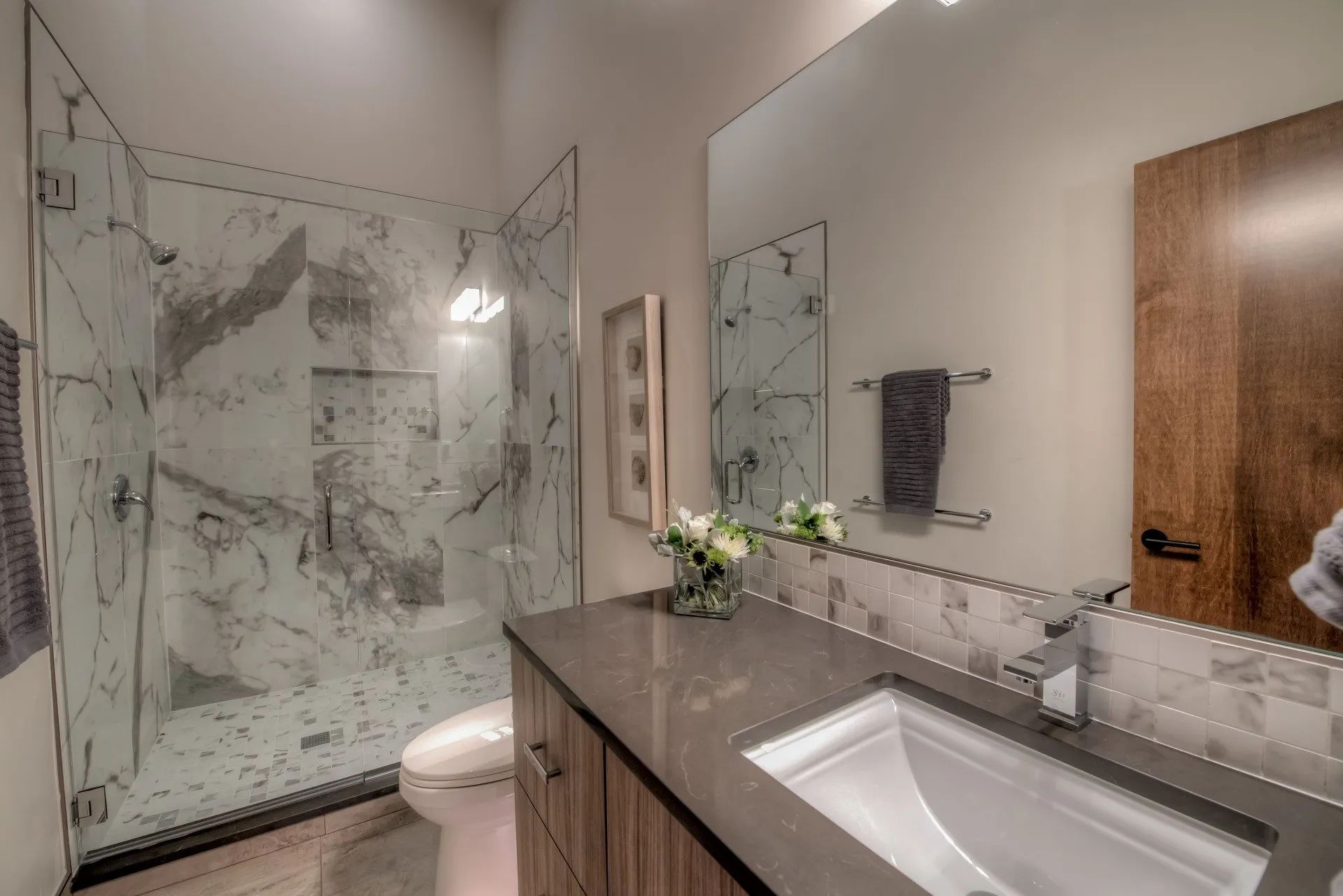 Modern bathroom with marble shower, vanity sink, mirror, and wooden door
