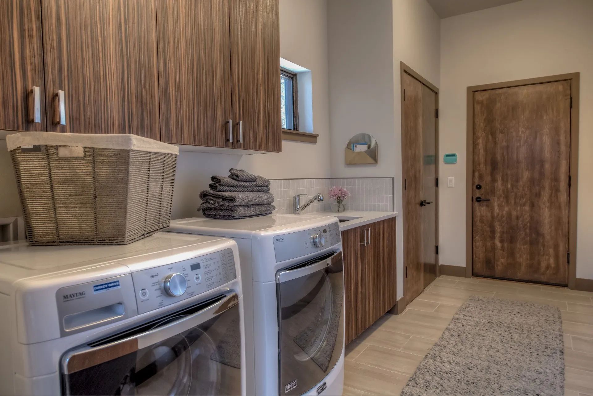 Laundry room with washer and dryer, wood cabinets, wicker baskets, and a beige runner rug.