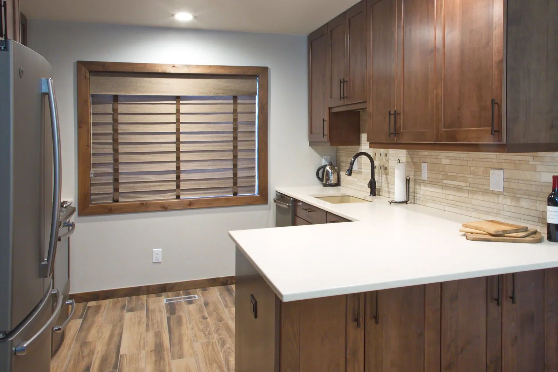 Modern kitchen with wood cabinets, white island, stainless fridge, and window blinds