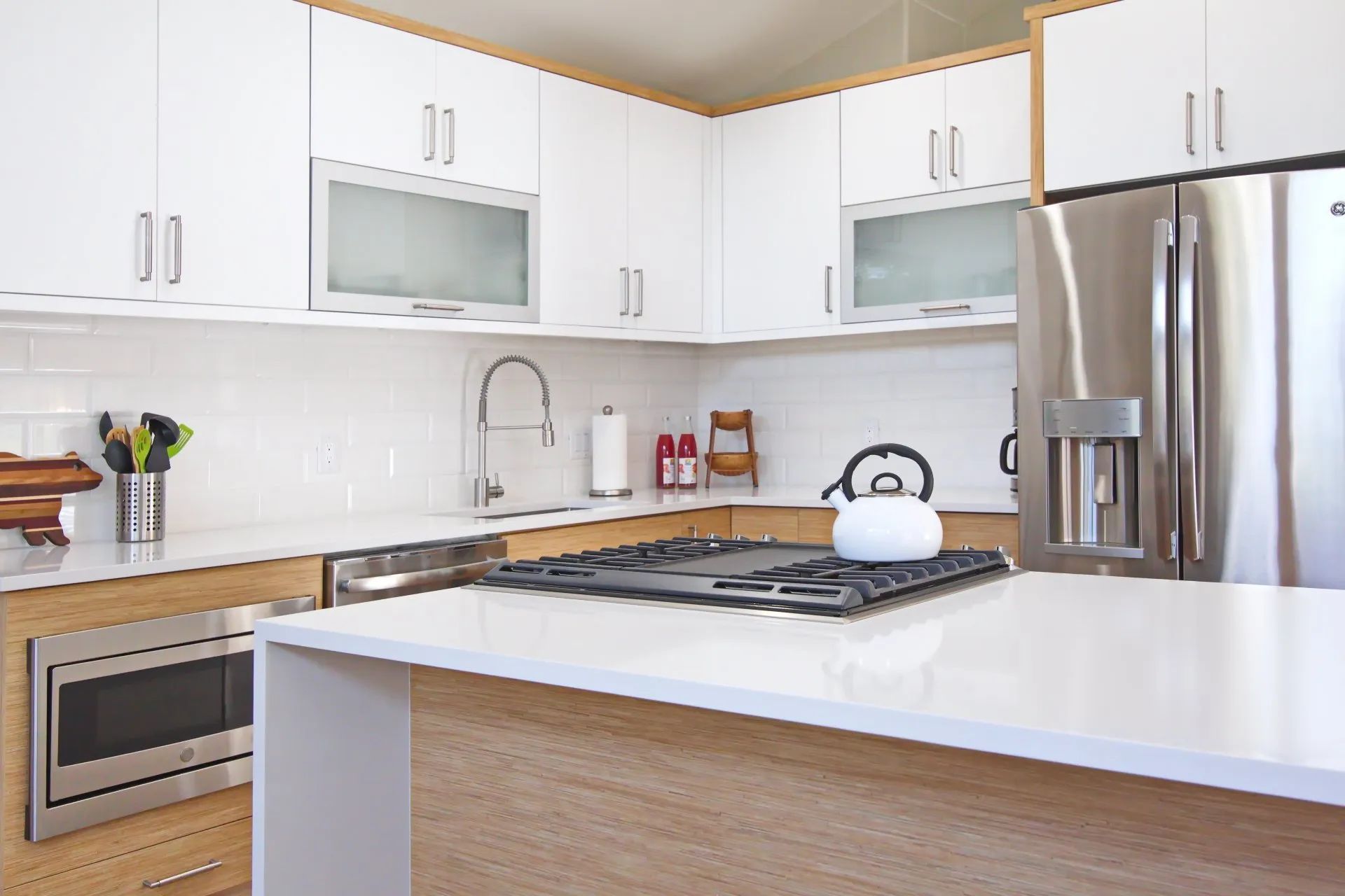 Modern white kitchen with island, stainless steel appliances, and a stove with a white kettle.