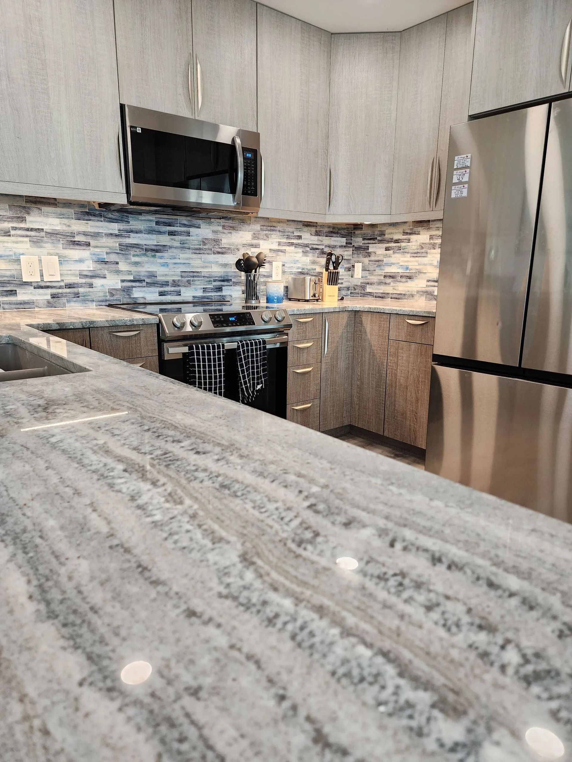 Modern kitchen with gray granite counters, stainless steel appliances, and blue-gray tile backsplash