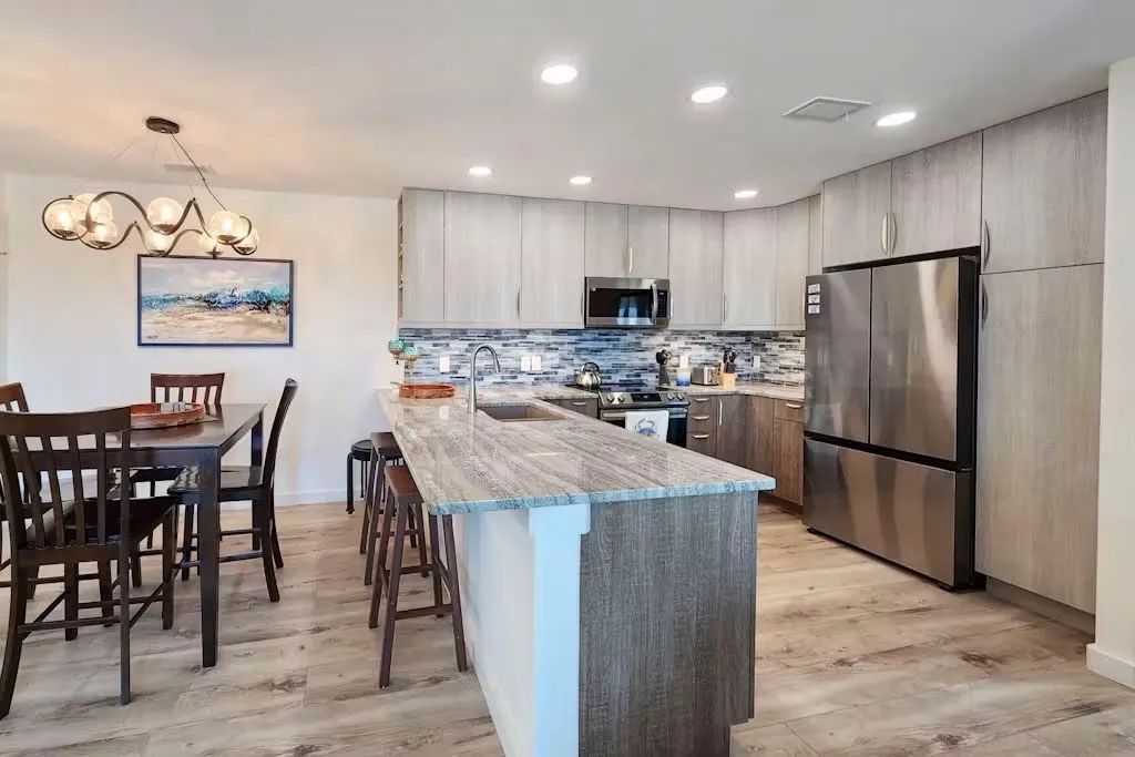 Modern kitchen with island, barstools, dining table, and stainless steel refrigerator.