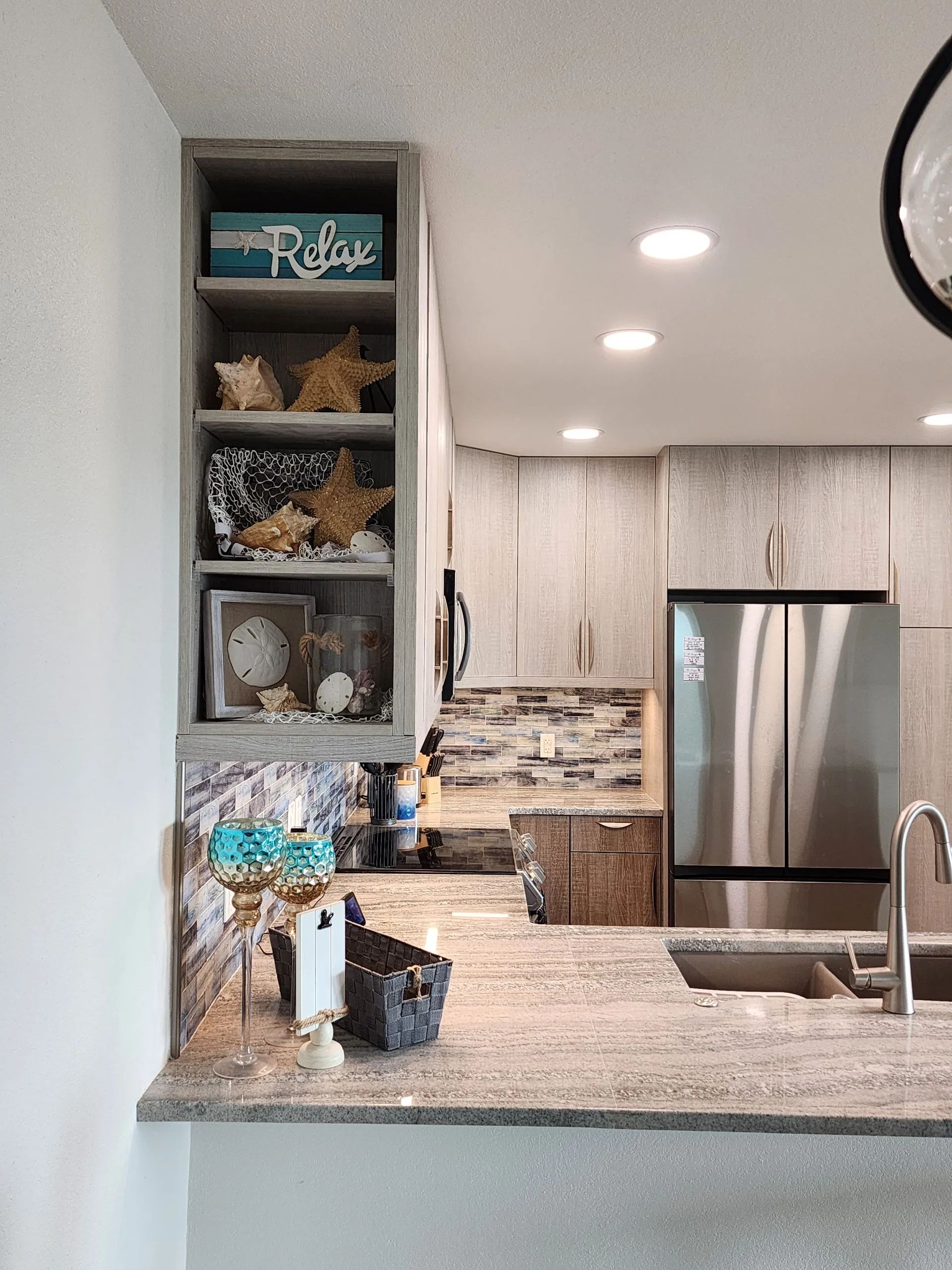 Modern kitchen with granite island, stainless steel fridge, open shelves, and recessed lighting
