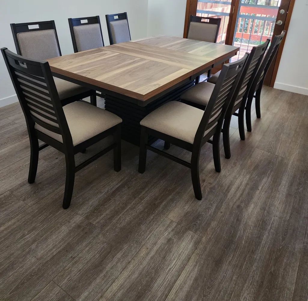 Wooden dining table with six chairs on a carpeted floor in a room with a bookshelf.