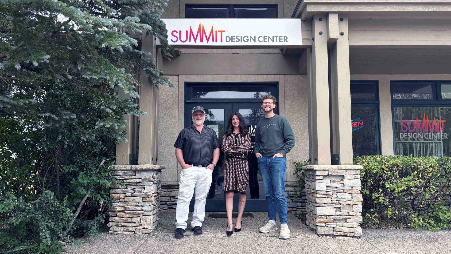 Three people standing at the entrance of SUMMIT Design Center, framed by stone pillars.