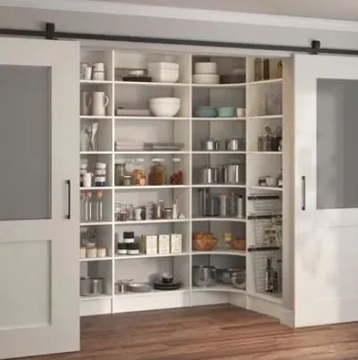 White kitchen pantry with open shelves stocked with dishes, jars, and bowls behind sliding doors