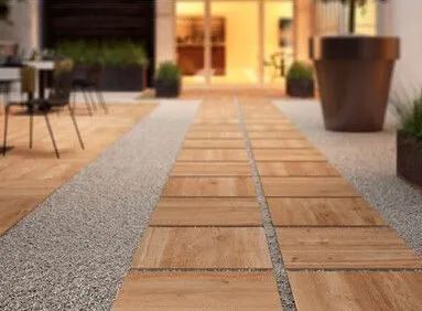 Modern patio walkway with tan wooden tiles and gray gravel borders, outdoors near seating and large planters