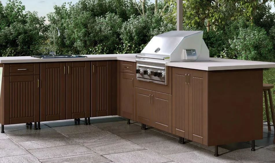 Outdoor stainless steel grill island with brown cabinets on a patio, surrounded by trees