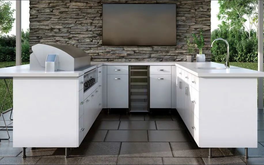 Outdoor kitchen with white cabinets, stone wall, built-in grill, sink, and central wine cooler under a TV