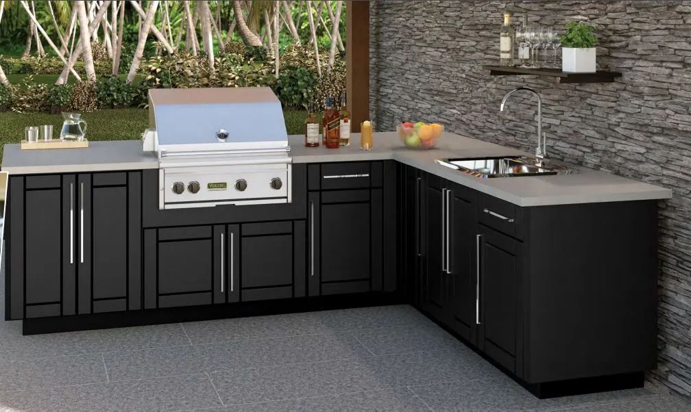Modern outdoor kitchen with black cabinets, stainless grill, stone backsplash, and countertop sink under bamboo backdrop