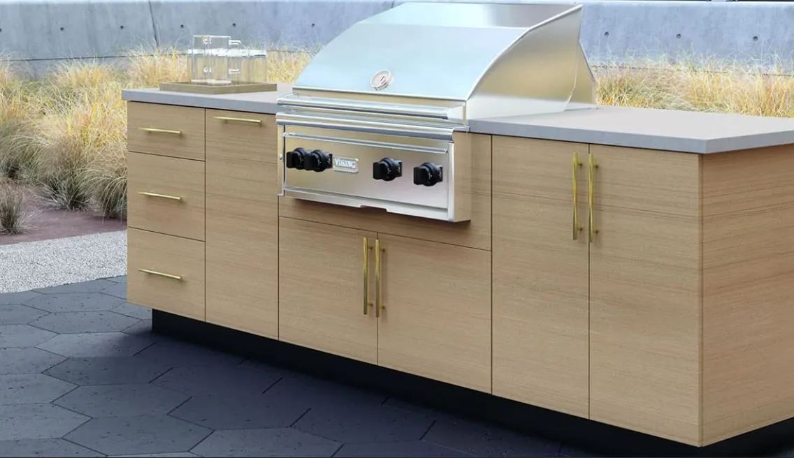 Outdoor built-in stainless steel grill island with light wood cabinets on a patio.