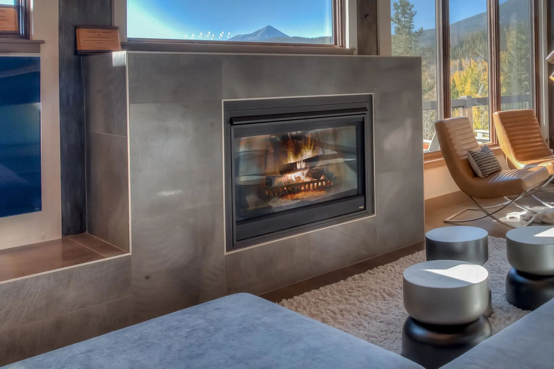 Modern living room with a glass fireplace, desert mountain view, and lounge chairs by a window.