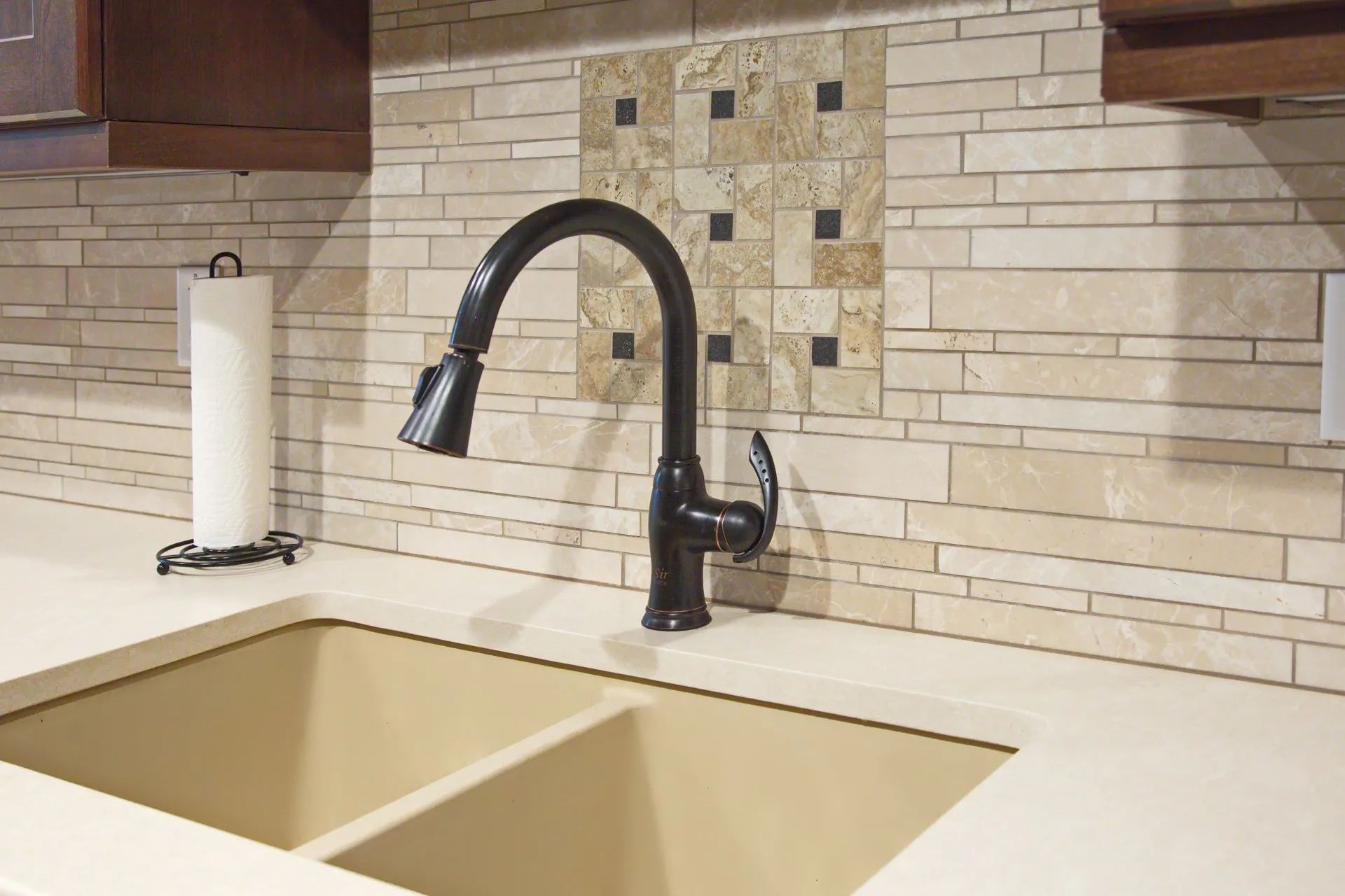 Kitchen sink with beige countertop, black faucet, and stone tile backsplash